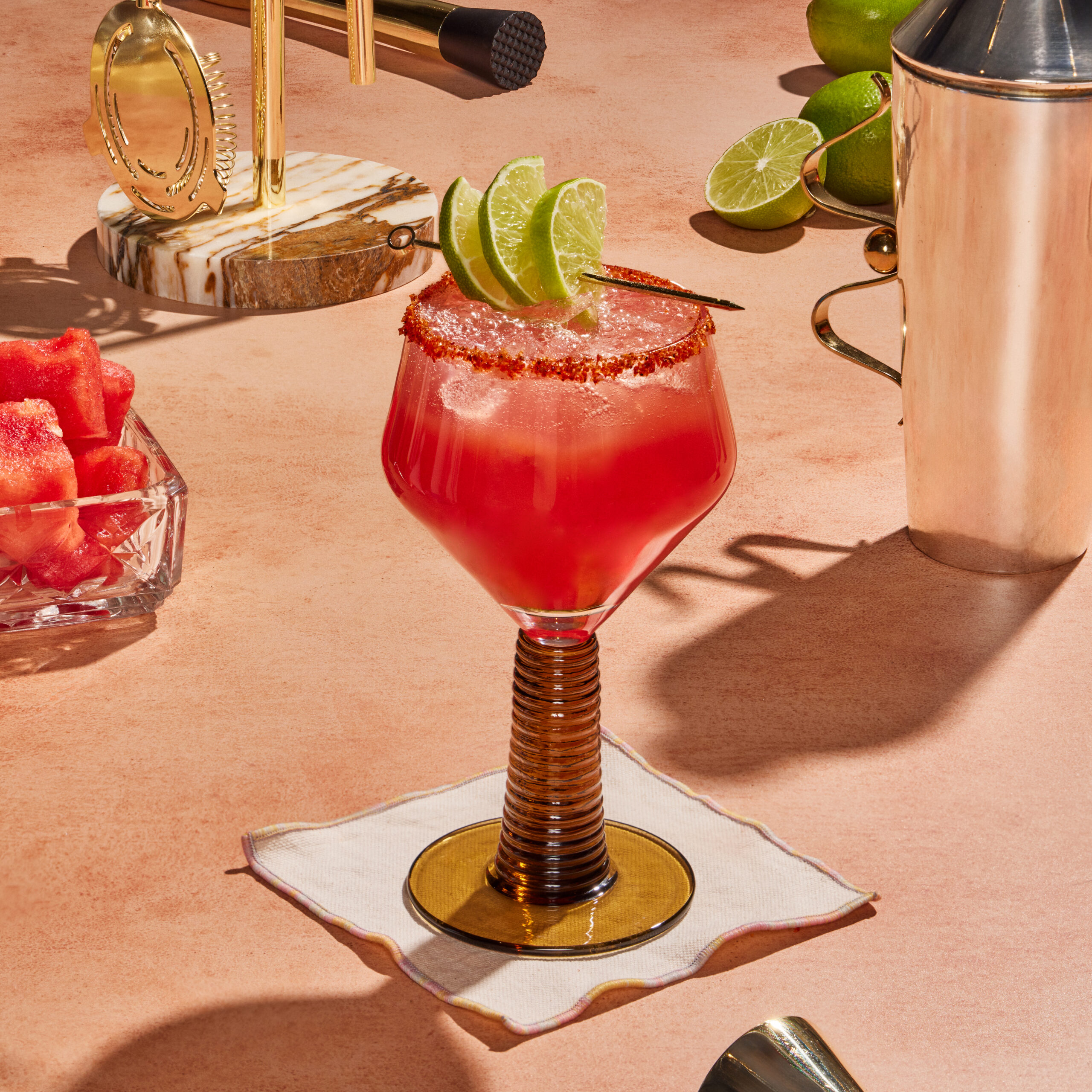 Spicy watermelon chamoy margarita with lime garnishes on a beige countertop.